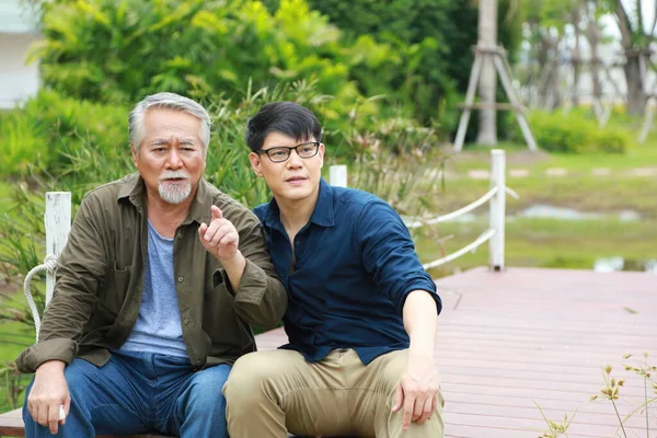 Happy old Asian man pass on his knowledge of life experience to his son while sitting together by the river pier with copy space