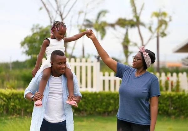 Family of African American people with young little daughter walking on green grass field while enjoying summer garden outside the house in the neighborhood with copy space