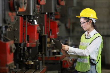 Güvenlik başlığı ve yansıtıcı bez giyen Asyalı kadın mühendis, dijital dizüstü bilgisayarla kopyalama alanı kullanarak fabrikanın içini inceliyor.