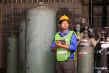 Asyalı endüstriyel işçiler, biyokimya endüstrisi için sıkıştırılmış konteynır tankında sıvı nitrojen ve argon önünde dururken fabrikadaki soğutucu sistemini kontrol etmek için dijital tablet kullanıyorlar.