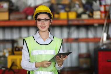 Güvenlik başlığı ve yansıtıcı bez içinde Asyalı mühendislik yöneticisi dijital tablet kullanarak fabrikanın içini kontrol ediyor.
