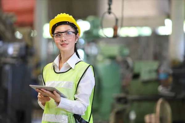 Güvenlik başlığı ve yansıtıcı bez içinde Asyalı mühendislik yöneticisi dijital tablet kullanarak fabrikanın içini kontrol ediyor.