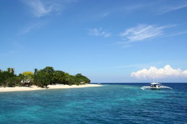 Derin mavi denizdeki ahşap tekne ve Balicasag adasının gökyüzü mercan kayalıkları, Panglao, Bohol, Filipinler için şnorkelle yüzme noktası