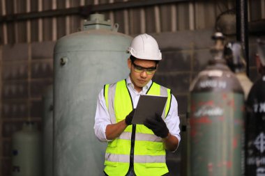 Asyalı endüstriyel işçiler, biyokimya endüstrisi için sıkıştırılmış konteynır tankında sıvı nitrojen ve argon önünde dururken fabrikadaki soğutucu sistemini kontrol etmek için dijital tablet kullanıyorlar.