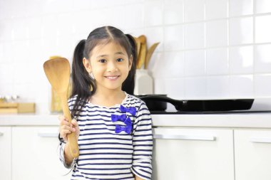 Modern mutfağın içinde spatulayla poz veren küçük Asyalı bir kız.