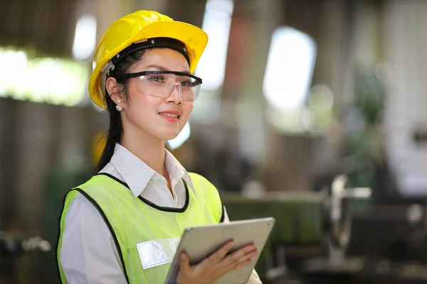 Asian engineering manager in safety hard hat and reflective cloth is inspecting inside the factory using digital tablet with copy space