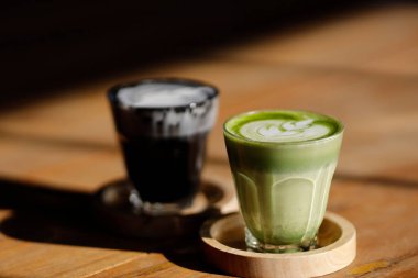 Bir fincan sıcak Japon kibrit yeşil sütlü latte. Lale desenli. Kırsal koyu ahşap masa üzerinde.