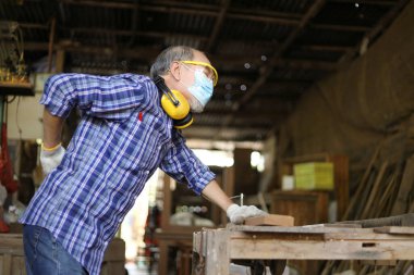 Kıdemli Asyalı marangoz, emeklilik çağında fotokopi alanında hobi olsun diye kendi garaj tarzı atölyesinde tahta keserken sırt ağrısı çekiyor.