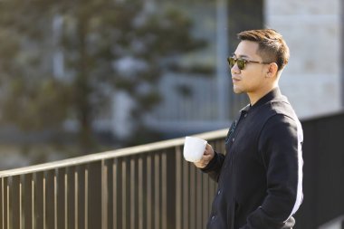 Spor giyimli Asyalı adam fotokopi odasıyla sabah egzersizinden sonra bir fincan kahve içiyor.