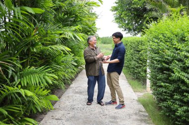 Kıdemli Asyalı bir adam oğluyla birlikte gülüyor ve baba oğul olarak kopyaladıkları komik anılardan bahsediyorlar.