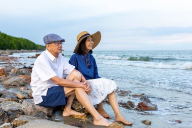 Asyalı yaşlı çift yaz tatillerinde sağlıklı bir ilişki ve emeklilik yıllarında mutlu bir evlilik hayatı için deniz sahilinde eğleniyor.