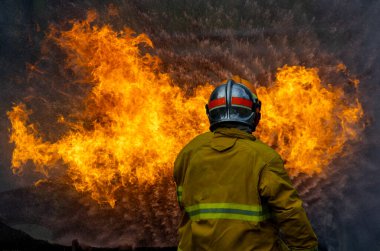 Yangın geçirmez giysili itfaiyeciler yangın söndürme görevi ve kaza yönetimi için yanan binayı yüksek alevlerle söndürmek için hortum kullanıyorlar.
