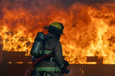 Yangın geçirmez elbiseli itfaiyeci yangın söndürme ve kaza kurtarma görevi ve kaza yönetimi için yanan binayı yüksek alevlerle söndürmek için hortum kullanıyor.