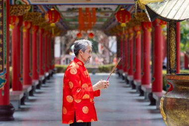 Kırmızı Cheongsam Qipao elbisesi giyen Asyalı son sınıf öğrencisi, Çin Budist tapınağındaki atalarımızın tanrısına tütsü sunuyor. Yeni yıl boyunca en iyi dilekler ve iyi şans konsepti için.