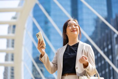 Şehir merkezindeki gökdelen caddesi modern ofisinde iş iletişimi ve kentsel yaşam tarzı üzerine yürürken cep telefonu kullanan lüks genç Asyalı CEO kadın girişimci.