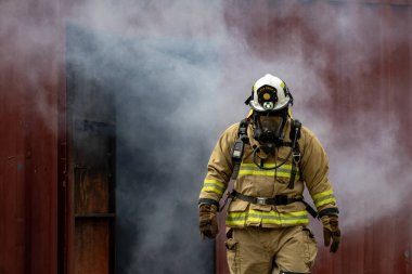 Yanmaz giysili itfaiyecinin portresi kül ve duman dolu binadan çıkarken yangın söndürme operasyonu ve kaza yönetimi riskini ortadan kaldırır.