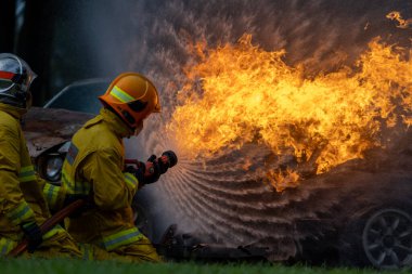 Yangın geçirmez giysili itfaiyeciler yangın söndürme görevi ve kaza yönetimi için yanan binayı yüksek alevlerle söndürmek için hortum kullanıyorlar.