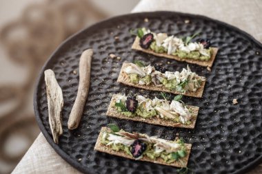 El yapımı siyah tabak, keten masa örtüsü ve ahşap aksesuarlar üzerinde bir ısırık deniz mahsulü atıştırmalığı.