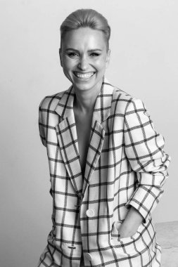 Zarif, karizmatik, sarışın ve kısa saçlı güzel geniş gülüşlü, büyük beden keten takım elbiseli, stüdyoda soyutlanmış poz veren kadınlar. Siyah ve beyaz versio