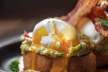 İki porsiyon Benedict usulü yumurta, kıtır jambon, haşlanmış yumurta ve kırsal kahverengi tabakta Hollandez sosu.