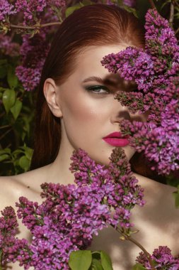 Genç manken portresi, ıslak kızıl saçlı, mavi gözlü ve çiçek açan leylak bahçeli güzel tenli.