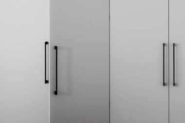 Siyah metal saplı İskandinav tarzı bir dolabın gri cephesi ve iç kısımda yarı açık bir kapı..