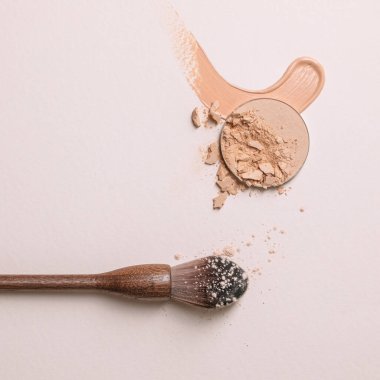 Çarpışan bej yüzler, sıvı toz ve sıfır atık ahşap barut fırçası. Bej arkaplanda makro makyaj dokusu