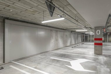 Empty public underground parking lot or garage interior with concrete stripe painted columns and signs
