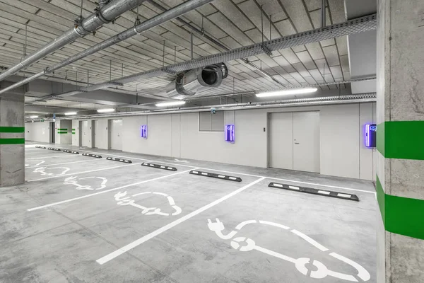 Empty public underground parking lot or garage interior with concrete stripe painted columns and signs. Electric car charging place.