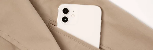 Modern smart phone in cream colour in the pocket of beige trench coat