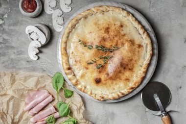 İtalyan calzone pizzası, mozzarella, jambon, mermer tepside fesleğen. Gri taşlı arka planda pizza malzemeleriyle süslenmiş. 