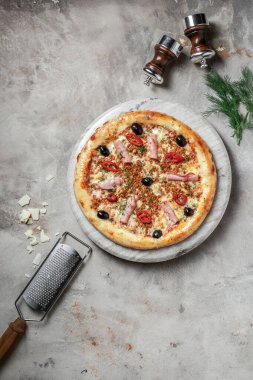 Jambonlu lezzetli pizza, mozzarella, mermer tepside kıyma. Gri taşlı arka planda pizza malzemeleriyle süslenmiş. 