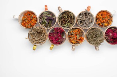 Beyaz arka planda renkli fincanlarda kurutulmuş gevşetici çay otları. Calendula, nane, anason hyssop, monarda didyma, pelin otu, adaçayı yaprakları..