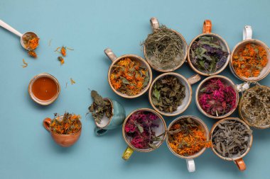Mavi arka planda renkli fincanlarda kurutulmuş gevşetici çay otları ve yakın planda bal. Calendula, nane, anason hyssop, monarda didyma, pelin otu, adaçayı yaprakları..