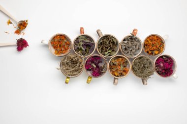Beyaz arka planda renkli fincanlarda kurutulmuş gevşetici çay otları. Calendula, nane, anason hyssop, monarda didyma, pelin otu, adaçayı yaprakları..