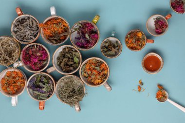Mavi arka planda renkli fincanlarda kurutulmuş gevşetici çay otları ve yakın planda bal. Calendula, nane, anason hyssop, monarda didyma, pelin otu, adaçayı yaprakları..