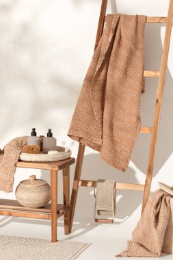 Doğal waffle keten havluları ahşap bankta toprak tonları ve bambu diş fırçaları, rattan sepetleri ve sabun makinesiyle havlu merdiveni. Günlük vücut bakımı, spa ve sıhhat sıfır atık tuvalet kavramı 