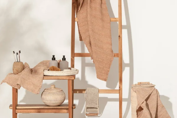 Doğal waffle keten havluları ahşap bankta toprak tonları ve bambu diş fırçaları, rattan sepetleri ve sabun makinesiyle havlu merdiveni. Günlük vücut bakımı, spa ve sıhhat sıfır atık tuvalet kavramı 