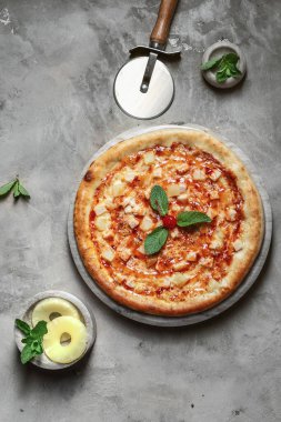 Tavuklu lezzetli pizza, mozzarella, mermer tepside ananas. Gri taşlı arka planda pizza malzemeleriyle süslenmiş. 