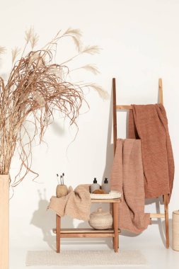 Doğal waffle keten havluları ahşap bankta toprak tonları ve bambu diş fırçaları, rattan sepetleri ve sabun makinesiyle havlu merdiveni. Günlük vücut bakımı, spa ve sıhhat sıfır atık tuvalet kavramı 