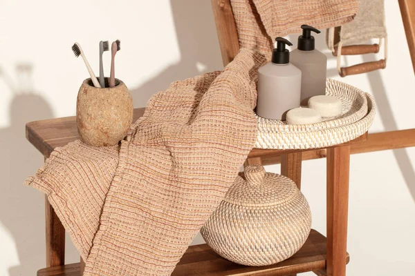 Doğal waffle keten havluları ahşap bankta toprak tonları ve bambu diş fırçaları, rattan sepetleri ve sabun makinesiyle havlu merdiveni. Günlük vücut bakımı, spa ve sıhhat sıfır atık tuvalet kavramı 