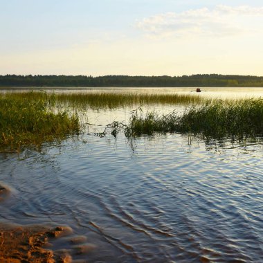 Gün batımında göl. Kıyıdan uzakta, yalnız bir tekne. 