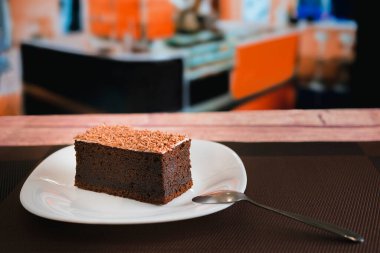 Kafeteryadaki ahşap masanın üzerinde ev yapımı lezzetli bir parça çikolatalı pasta ile tabağın arka planı bulanık.