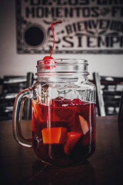 Kırmızı şaraplı, meyveli ve kirazlı bir bardak sodanın arka planı bulanık.