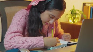 İspanyol genç, lise öğrencisi uzaktan öğretmenleriyle video görüşmesi yapmak için kulaklık takıyor, evden uzak dersler alıyor, sanal derslerinde öğrendiklerini not defterine yazıyor.