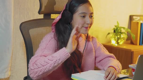 ヒスパニック系のティーンエイジャー 高校生は彼女の家族とビデオ通話を行うためにヘッドフォンを使用します 彼女は隔離された自宅です リモートの人々と彼女のラップトップの前で挨拶や会談 — ストック動画