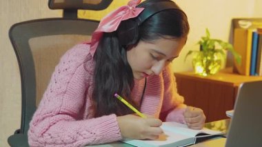 İspanyol genç, lise öğrencisi uzaktan öğretmenleriyle video görüşmesi yapmak için kulaklık takıyor, evden uzak dersler alıyor, sanal derslerinde öğrendiklerini not defterine yazıyor.