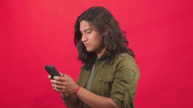 Adam akıllı telefonunu kontrol eder, mesajlarını görünce sinirlenir, kızgın bir ifade takınır ve onaylamayarak kollarını kavuşturur, kırmızı arka planı olan bir stüdyoda video çeker.