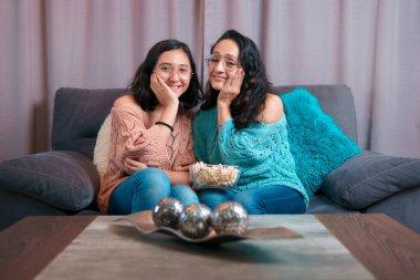 Evde film izleyen bir anne ve kızın yatay görüntüsü, patlamış mısır yiyorlar, ikisi de korkmuş ve çok farklı ifadeler sergiliyorlar.