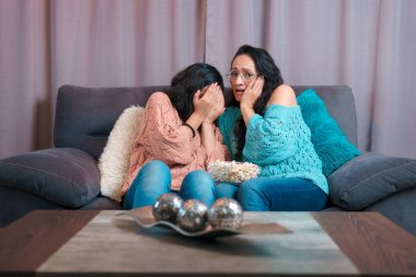 Evde film izleyen bir anne ve kızın yatay görüntüsü, patlamış mısır yiyorlar, ikisi de korkmuş ve çok farklı ifadeler sergiliyorlar.